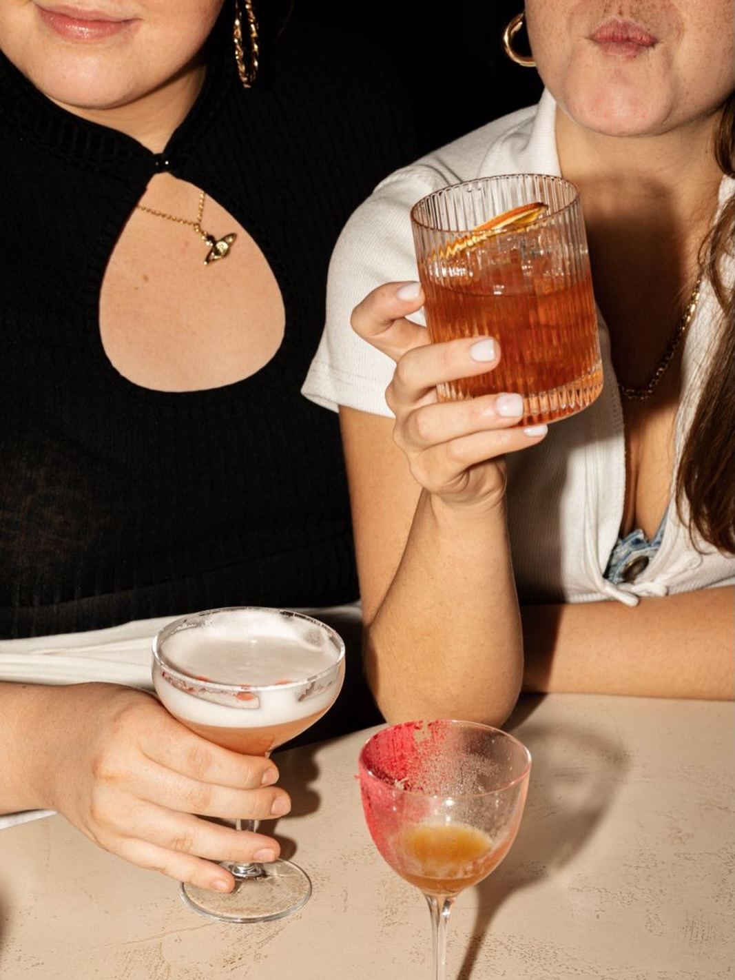 Two friends at the bar holding a cocktail and a sour