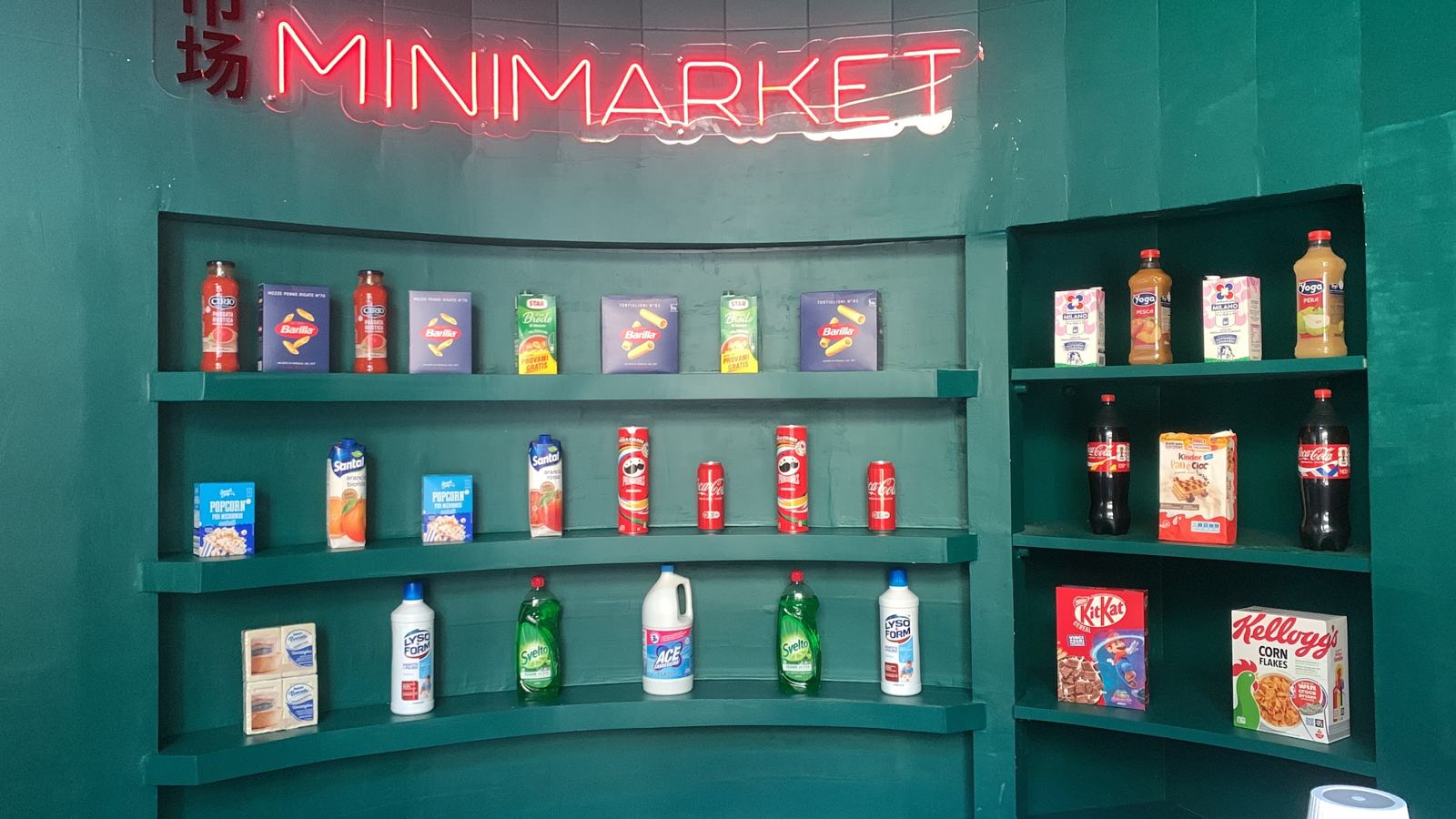The green wall with the Minimarket neon sign and shelves full of minimarket products