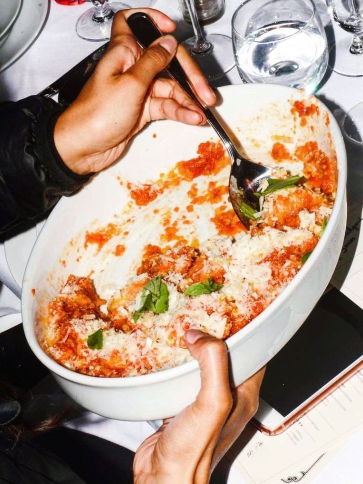 A dish of baked pasta with tomato and basil, served at the table
